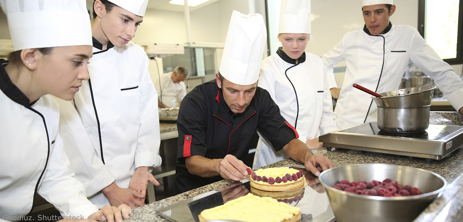 Four student chefs watching a teacher decorate a cake - Does a culinary school train students for jobs as chefs and cooks?